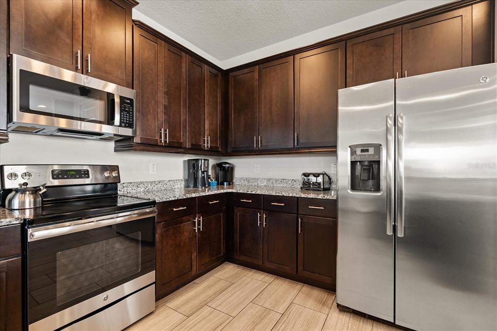 A kitchen with dark wood cabinets, stainless steel appliances, and granite countertops — 1113 CASTLE PINES COURT, REUNION, FL