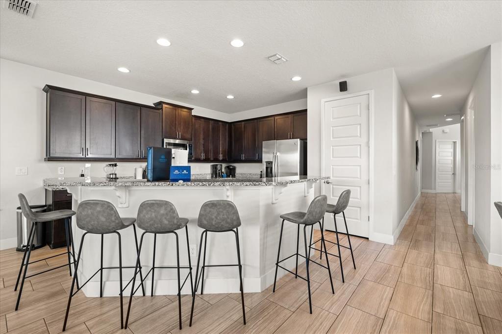 A kitchen features dark wood cabinets, granite countertops, a breakfast bar with stools, and tile flooring — 1113 CASTLE PINES COURT, REUNION, FL