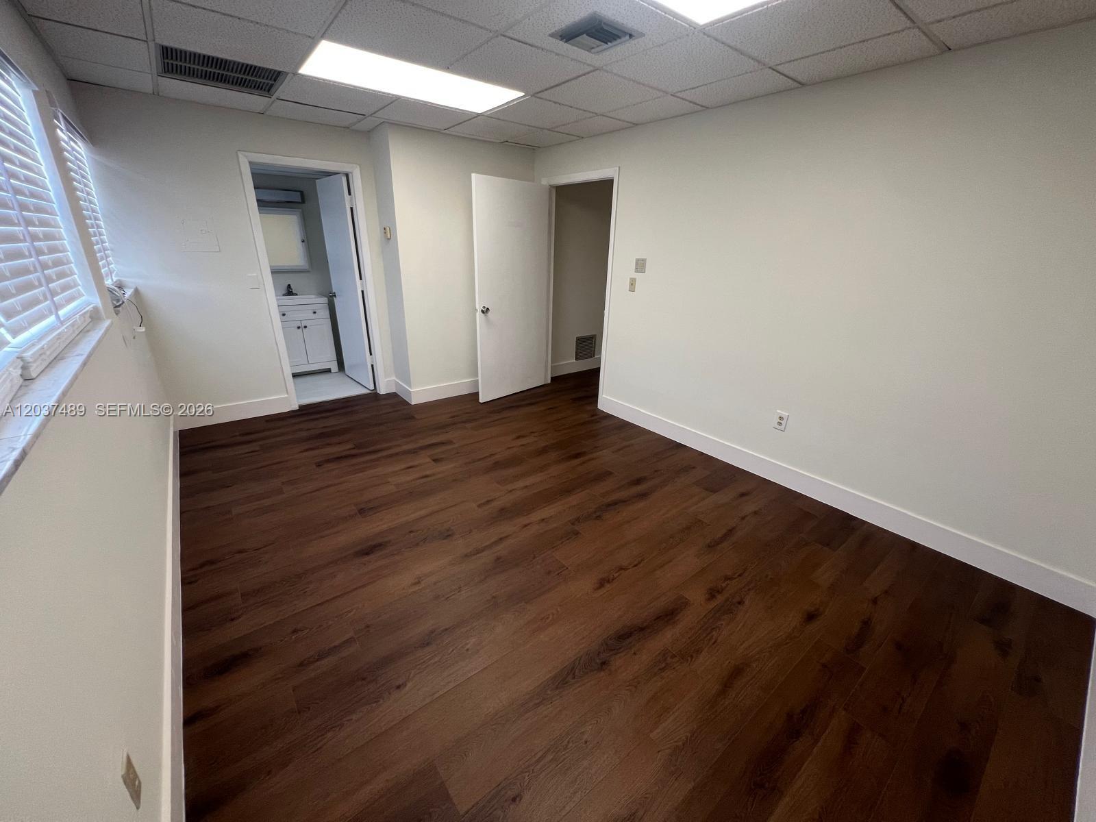An empty room features dark wood-look flooring, white walls, a drop ceiling, and two doorways — 145 Madeira Ave # 202, Coral Gables FL 33134, CORAL GABLES, FL