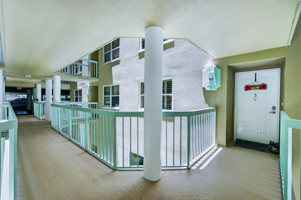 An outdoor apartment building walkway features a white door, light green railings, and a central pillar — 4 OCEANS WEST BOULEVARD UNIT 207A, DAYTONA BEACH, FL