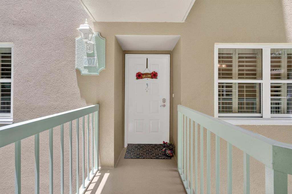 A white front door with a welcome sign is situated between two windows on a balcony — 4 OCEANS WEST BOULEVARD UNIT 207A, DAYTONA BEACH, FL
