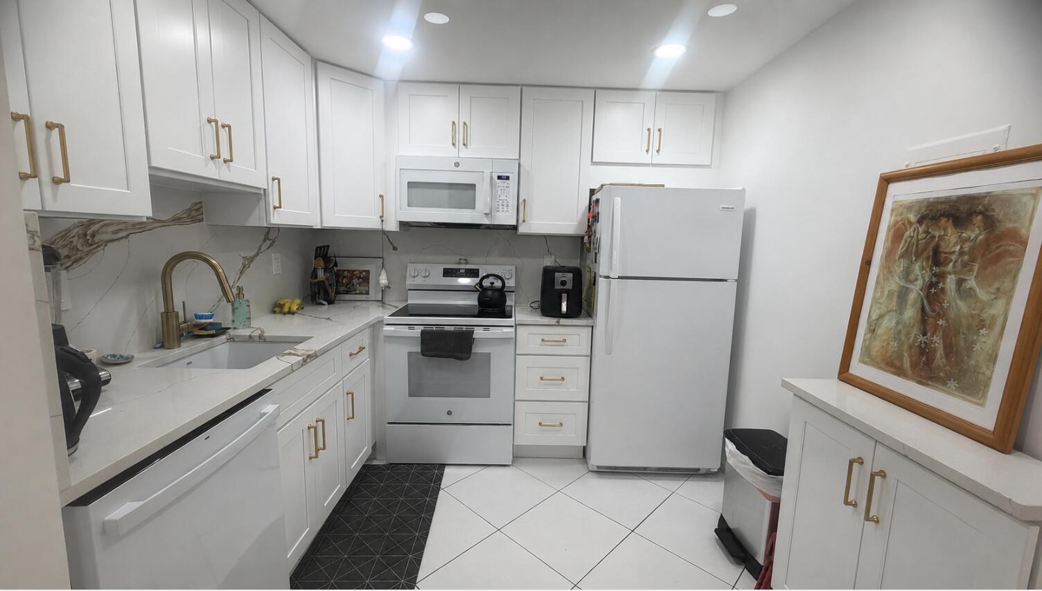 A white kitchen features gold hardware, quartz countertops, a tile backsplash, and white appliances — 930 Normandy, Delray Beach FL 33484, DELRAY BEACH, FL