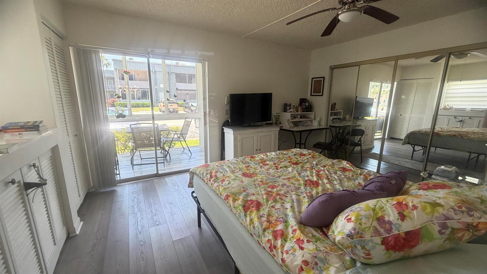 A bedroom features a floral bed, sliding glass doors to a patio, and mirrored closets — 930 Normandy, Delray Beach FL 33484, DELRAY BEACH, FL
