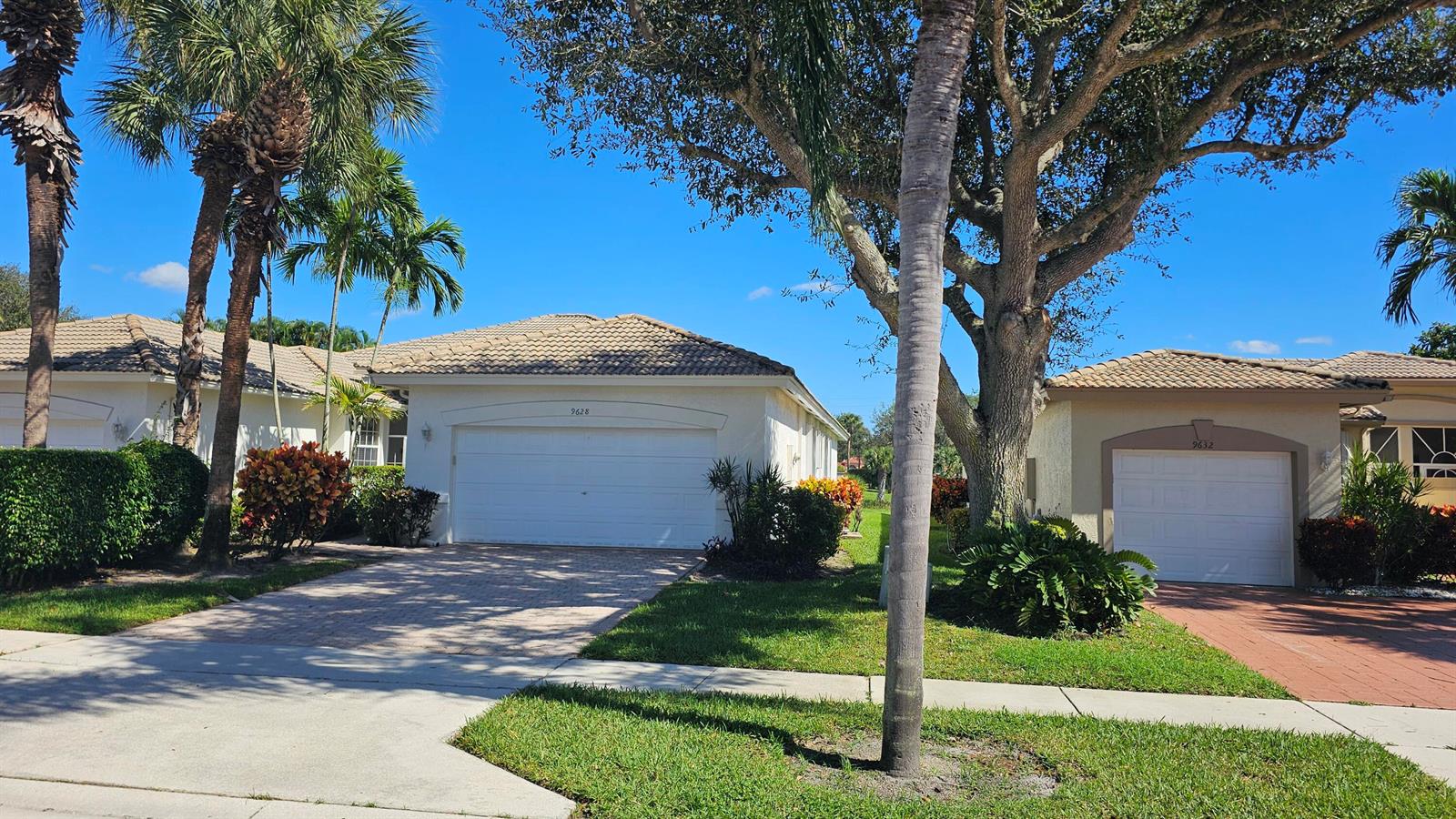 Two single-story houses with white garage doors and tiled roofs sit side-by-side under trees — 9628 Crescent View Drive N, Boynton Beach FL 33437, BOYNTON BEACH, FL