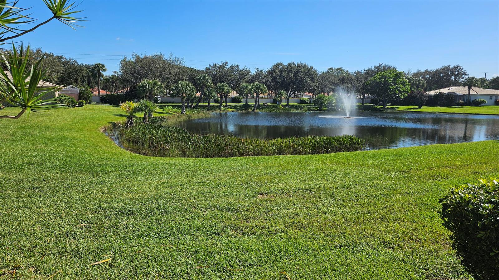 A grassy lawn leads to a pond with a fountain surrounded by trees and houses — 9628 Crescent View Drive N, Boynton Beach FL 33437, BOYNTON BEACH, FL