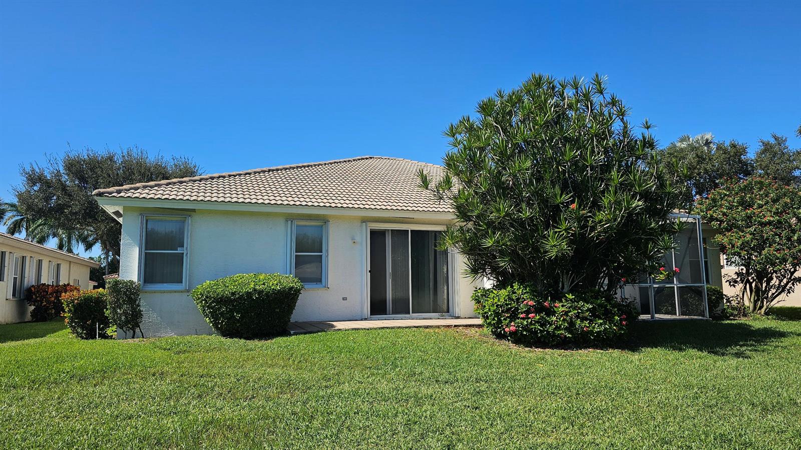 The exterior of a single-story house features a light-colored facade, a tiled roof, and landscaping — 9628 Crescent View Drive N, Boynton Beach FL 33437, BOYNTON BEACH, FL