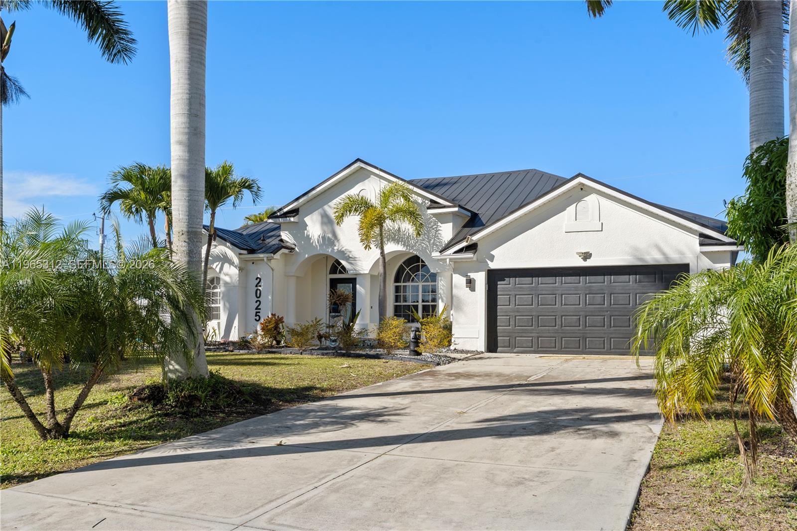 A single-story white house with a dark garage door and palm trees in the front yard — 2025 NW 7th ter, Cape Coral FL 33993, CAPE CORAL, FL