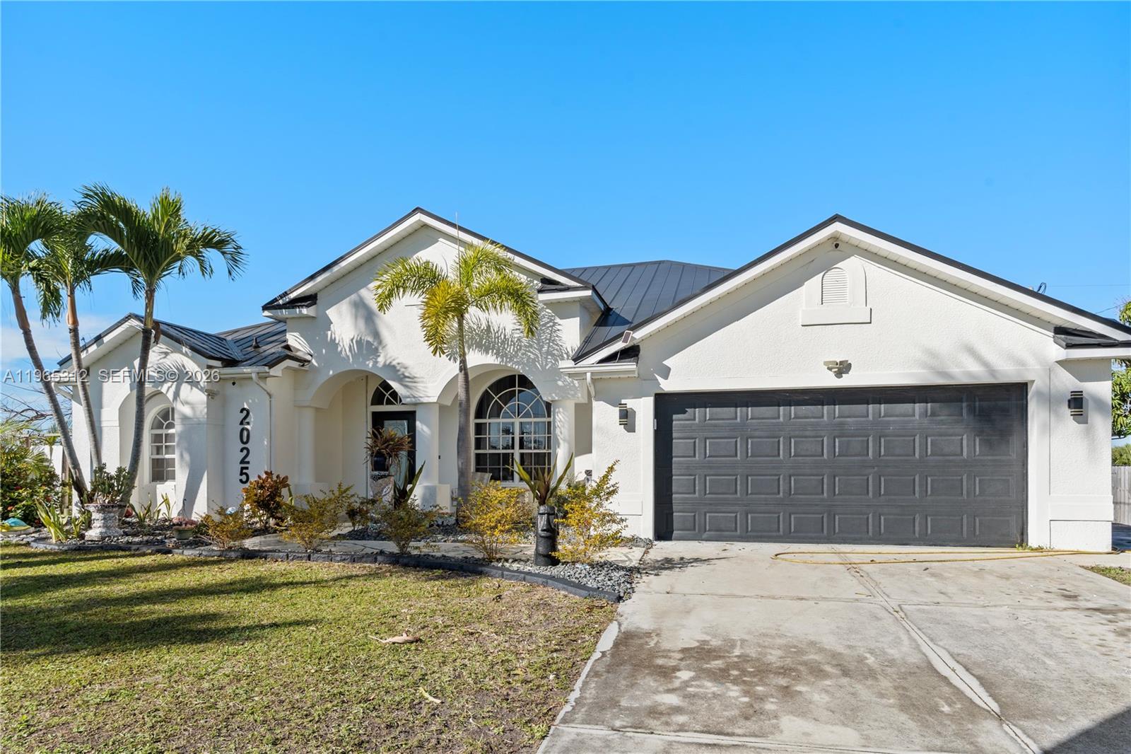 A white single-story house with a dark metal roof and a two-car garage — 2025 NW 7th ter, Cape Coral FL 33993, CAPE CORAL, FL