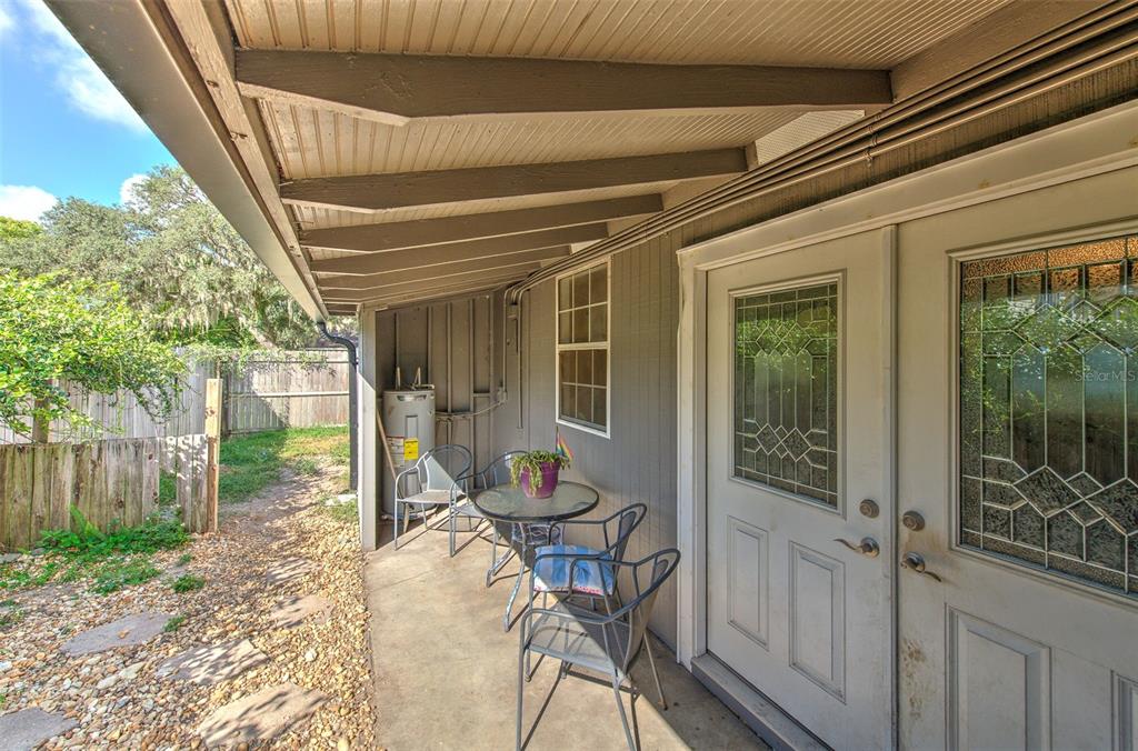 A covered patio features a small table with chairs, a water heater, and double doors — 38708 9TH AVENUE, ZEPHYRHILLS, FL