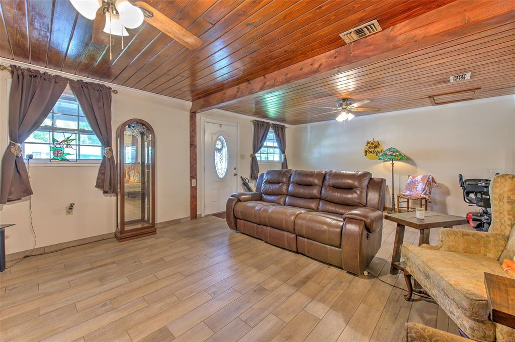 A living room features wood-paneled ceilings, tile flooring, a brown leather sofa, and a front door — 38708 9TH AVENUE, ZEPHYRHILLS, FL