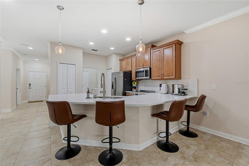 A kitchen features a white countertop island with four brown bar stools and wooden cabinets — 3550 FAIRWATERS COURT UNIT #C, CLERMONT, FL
