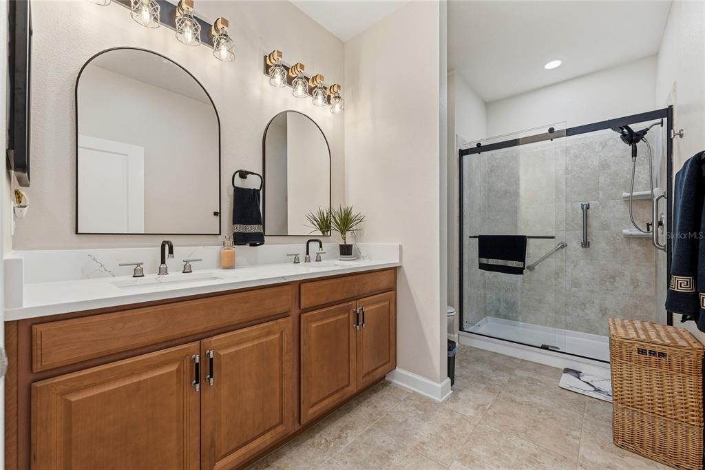 A bathroom features a double-sink wood vanity, arched mirrors, and a glass-enclosed walk-in shower — 3550 FAIRWATERS COURT UNIT #C, CLERMONT, FL