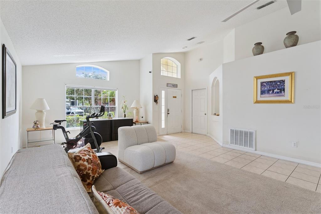 A living room features a vaulted ceiling, tiled entryway, carpeted seating area, and an exercise bike — 126 MADIERA BEACH BLVD, KISSIMMEE, FL