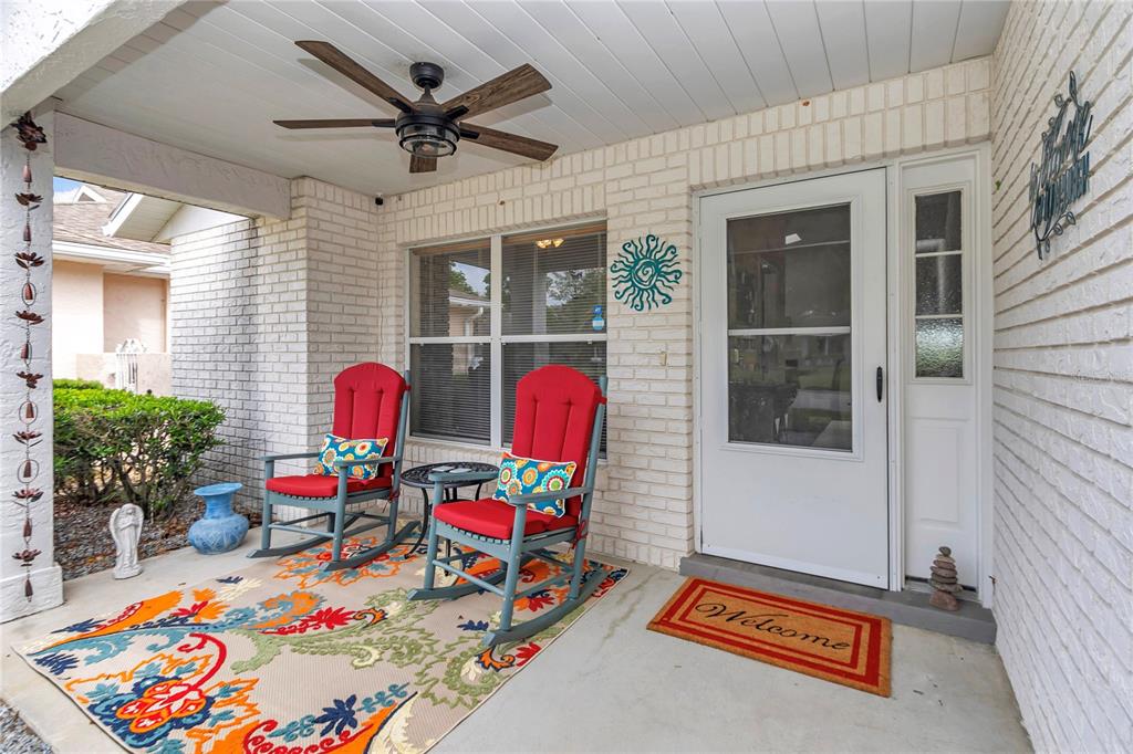 A covered front porch features two red rocking chairs, a patterned rug, and white brick — 9185 SW 90TH STREET, OCALA, FL