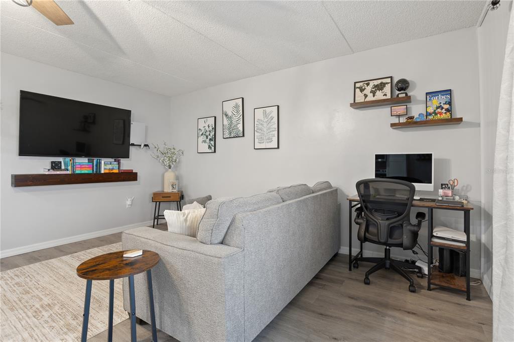 A living room features a grey sofa, a wall-mounted television, and a small desk area — 1154 PASEO DEL SOL UNIT B, CASSELBERRY, FL
