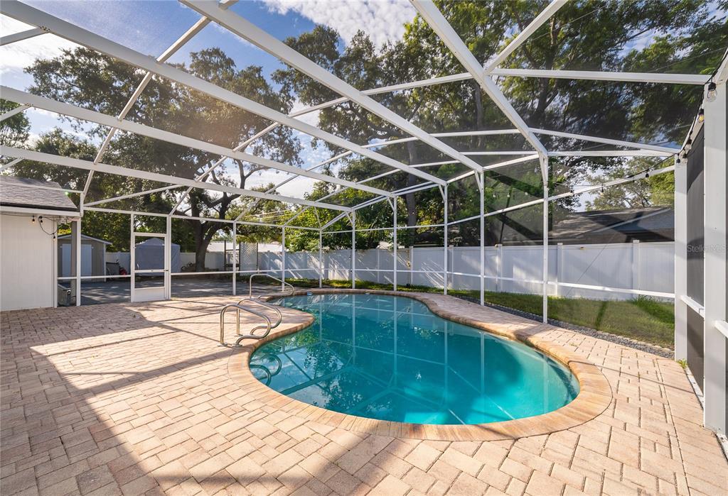 A screened-in backyard patio features a kidney-shaped swimming pool surrounded by light-colored brick pavers — 2462 CAROLTON ROAD, MAITLAND, FL