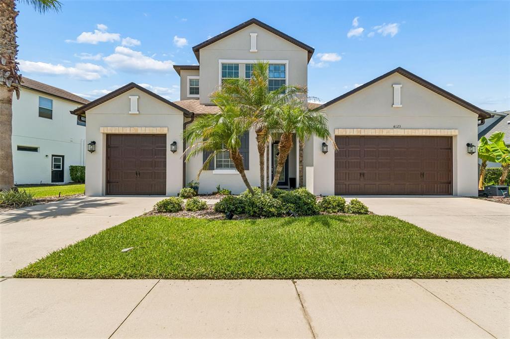 A two-story suburban house features a three-car garage, a palm tree, and a front lawn — 4123 WINDCREST DRIVE, WESLEY CHAPEL, FL