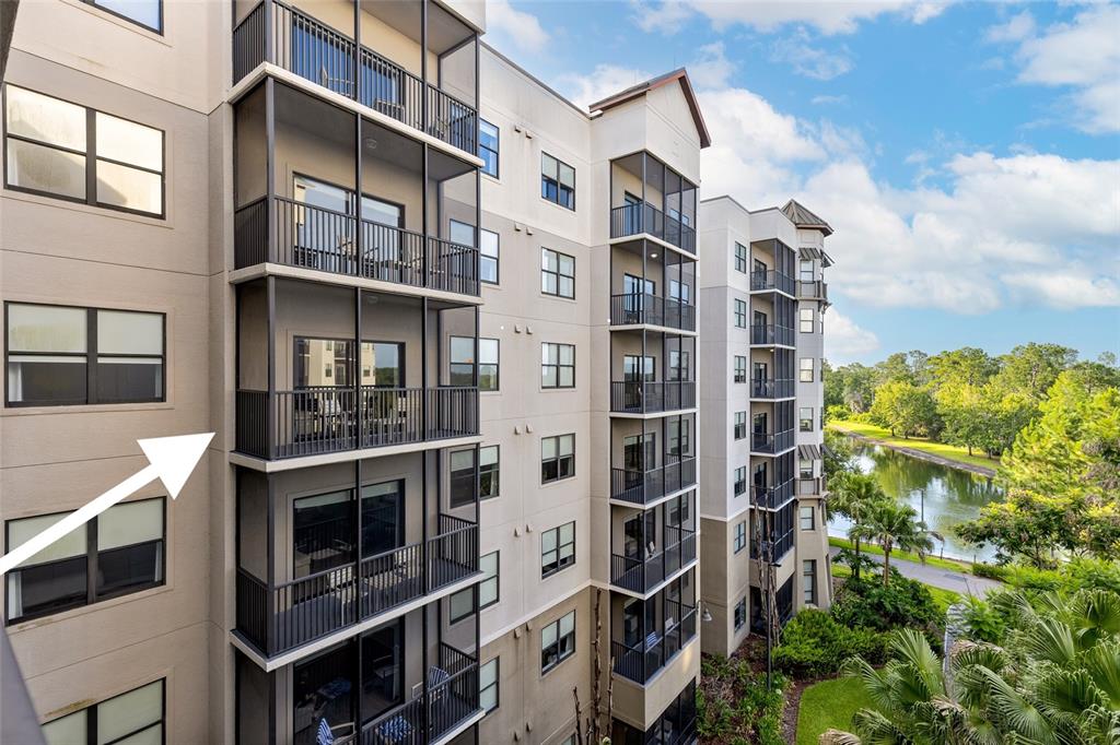 An exterior view of a multi-story apartment building featuring screened-in balconies overlooking a pond — 14501 GROVE RESORT AVENUE UNIT 1527, WINTER GARDEN, FL