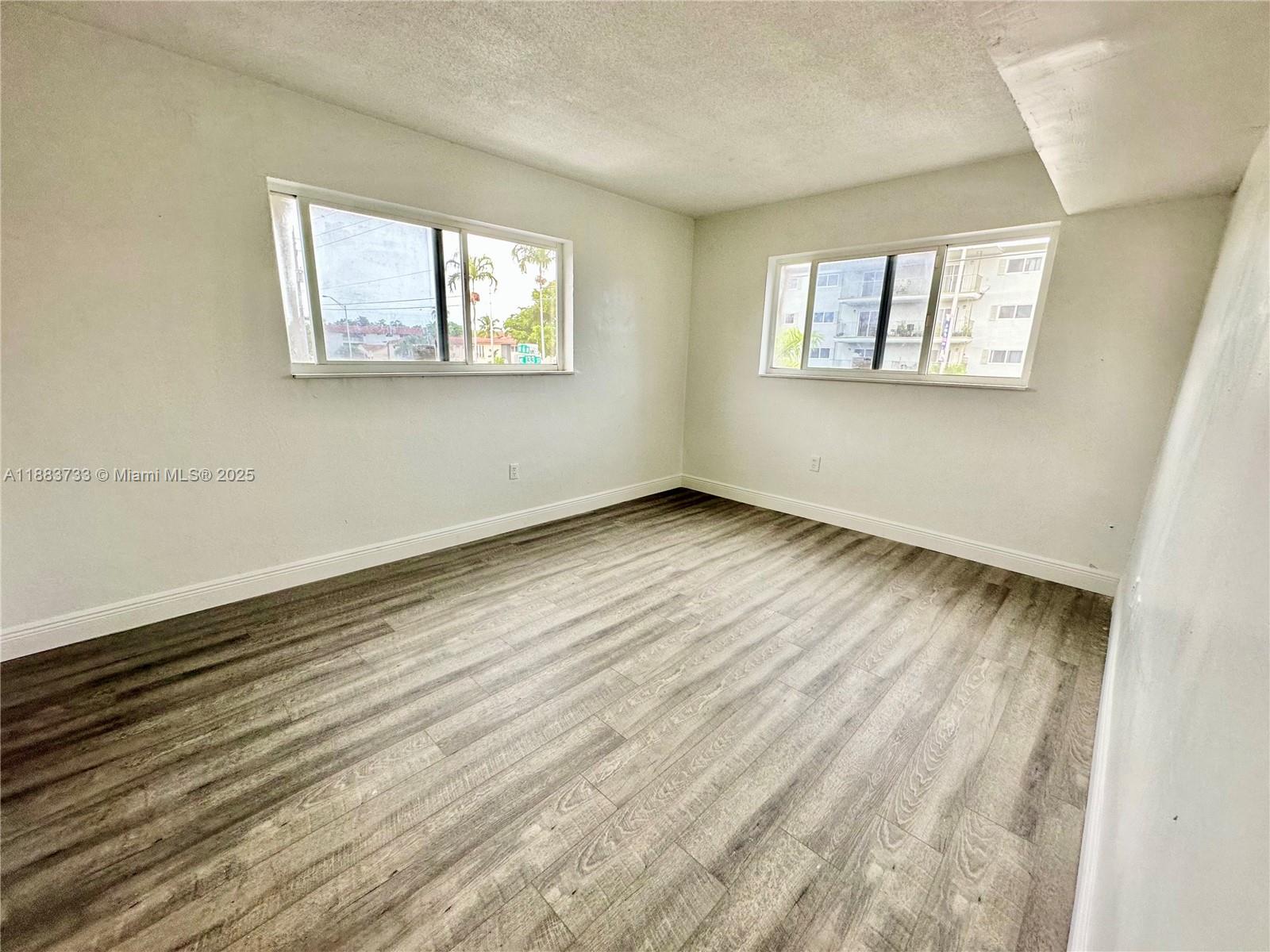 An empty room features light-colored walls, wood-look flooring, and two windows — 13285 NE 6th Ave # 109, North Miami FL 33161, NORTH MIAMI, FL