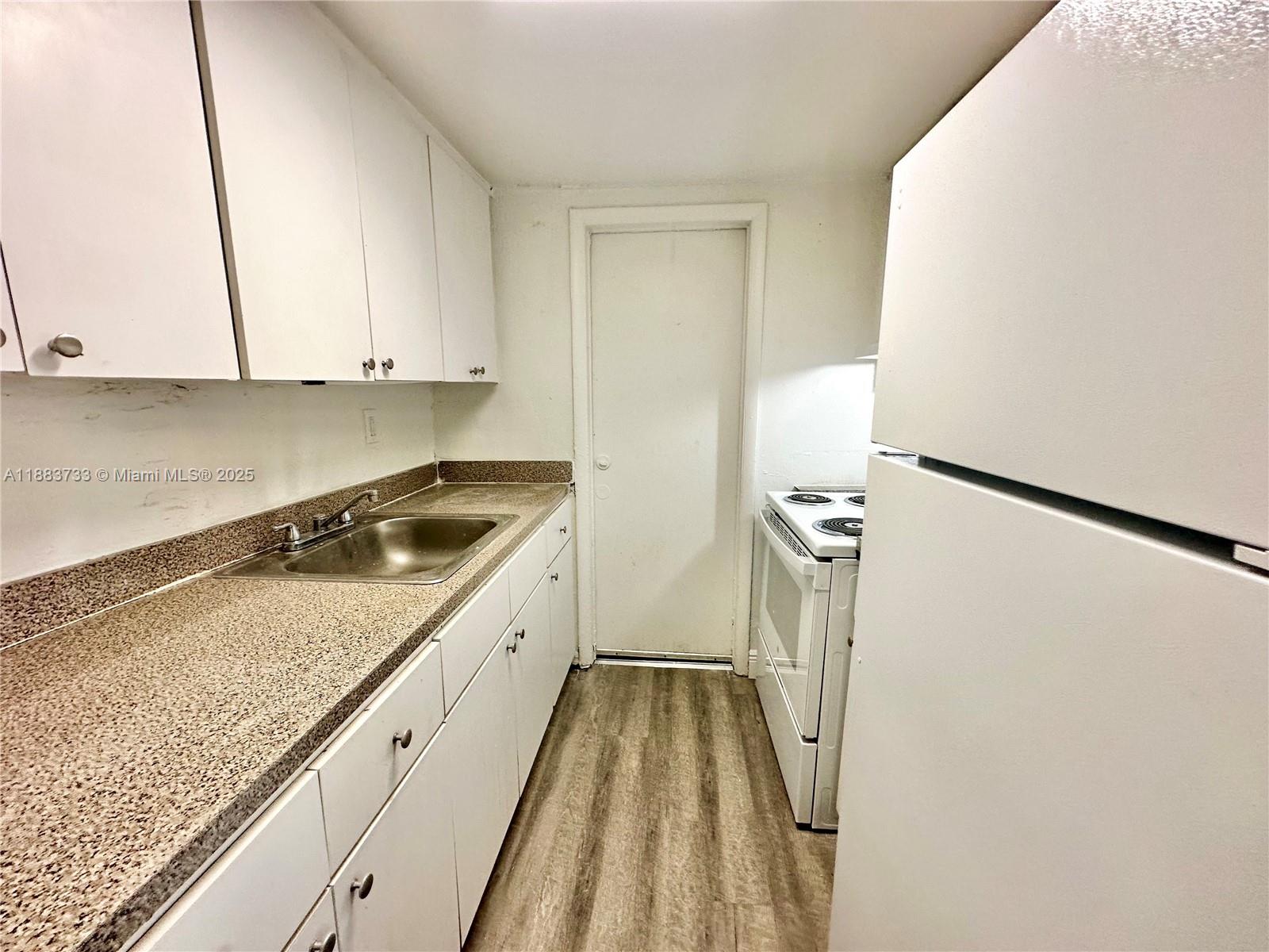 A galley kitchen features white cabinets, speckled countertops, a stainless steel sink, and wood-look flooring — 13285 NE 6th Ave # 109, North Miami FL 33161, NORTH MIAMI, FL
