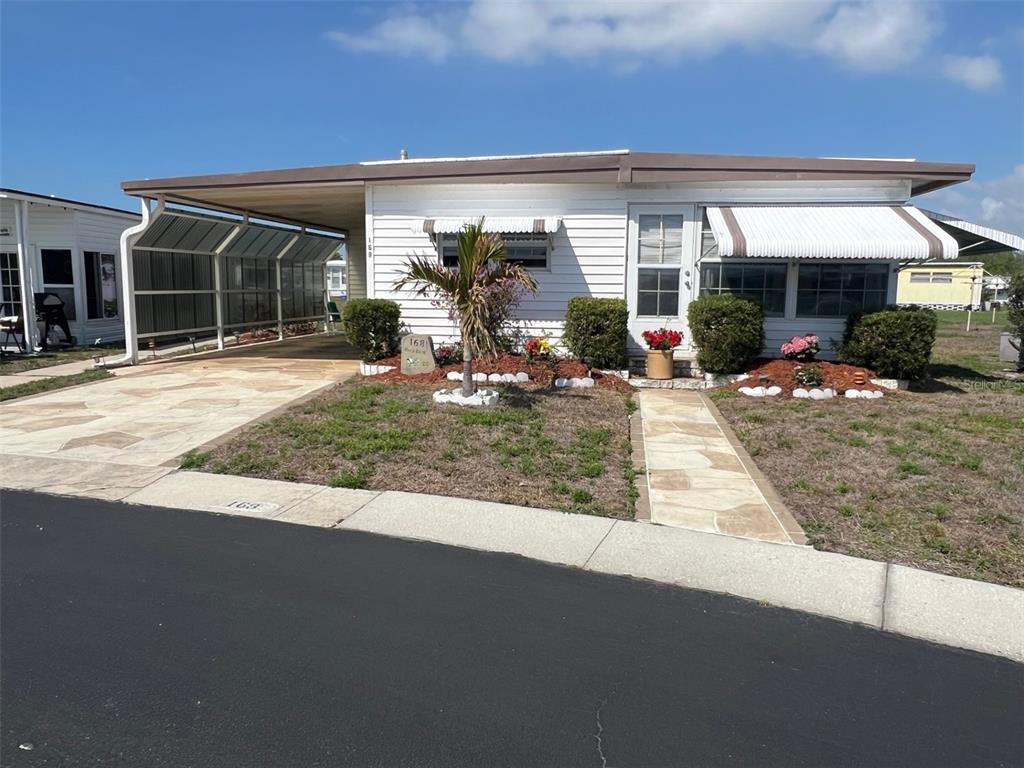 A single-story mobile home with a carport, white siding, and a stone walkway — 13225 101ST STREET UNIT 168, LARGO, FL