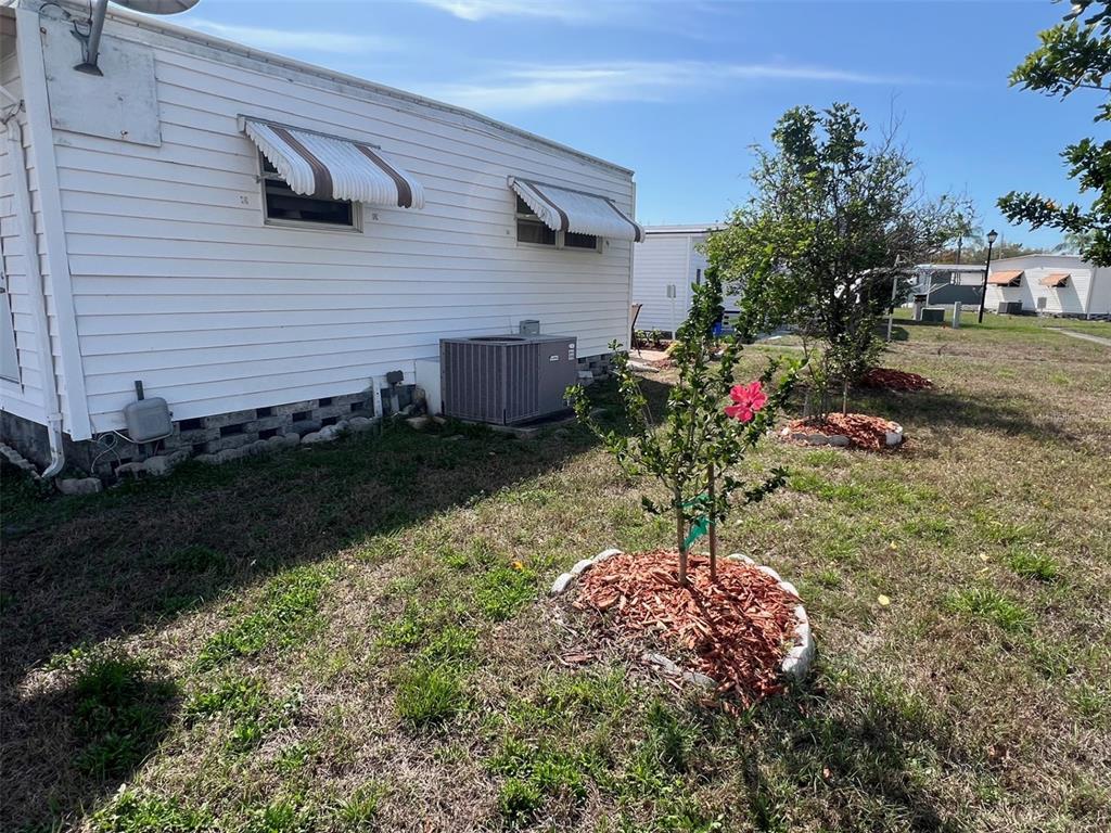 A white mobile home exterior features two window awnings, an HVAC unit, and landscaped trees — 13225 101ST STREET UNIT 168, LARGO, FL
