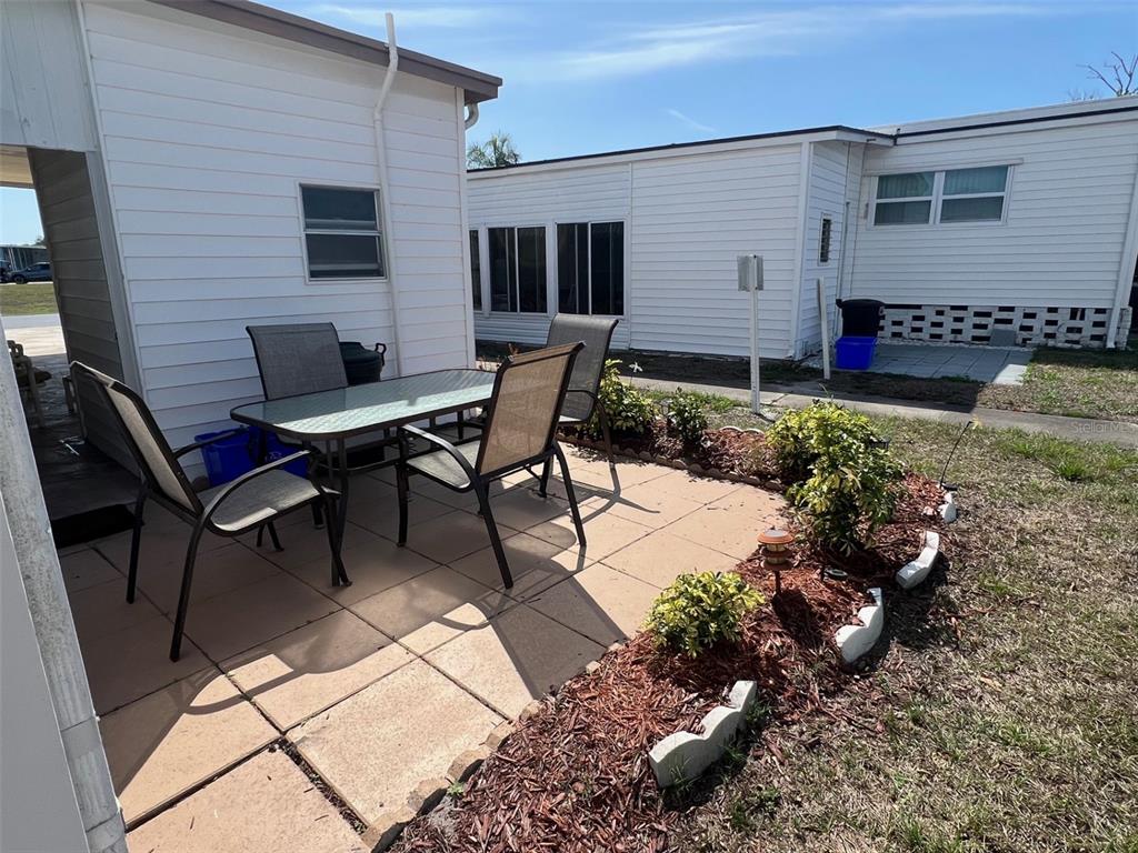 A patio with a glass-top table and chairs sits between two white mobile homes — 13225 101ST STREET UNIT 168, LARGO, FL