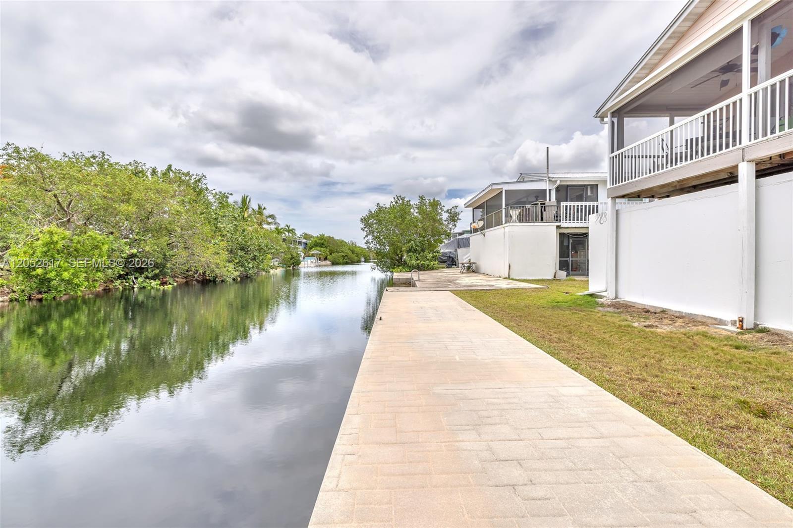 A paved walkway runs along a canal next to a house with a screened porch — LOWER KEYS, FL