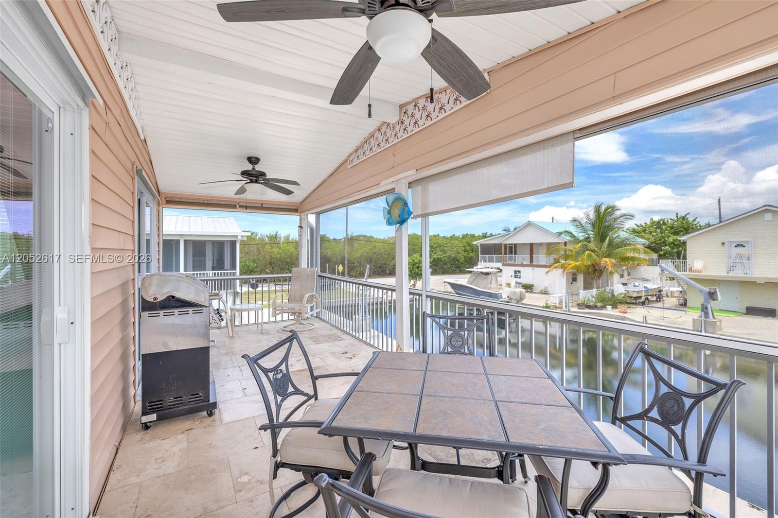A covered balcony features a dining set, a grill, and a view of a canal — LOWER KEYS, FL