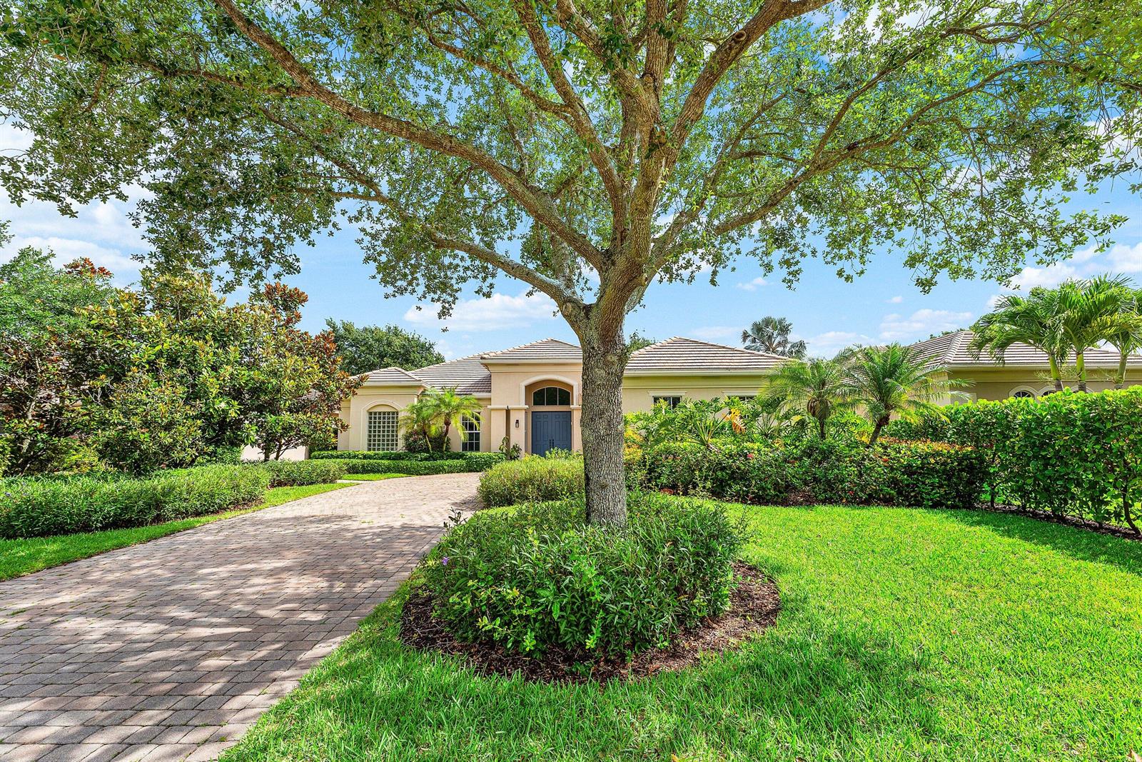 A paved driveway leads to the entrance of a single-story house shaded by a large tree — 2068 Wightman Drive, Wellington FL 33414, WELLINGTON, FL