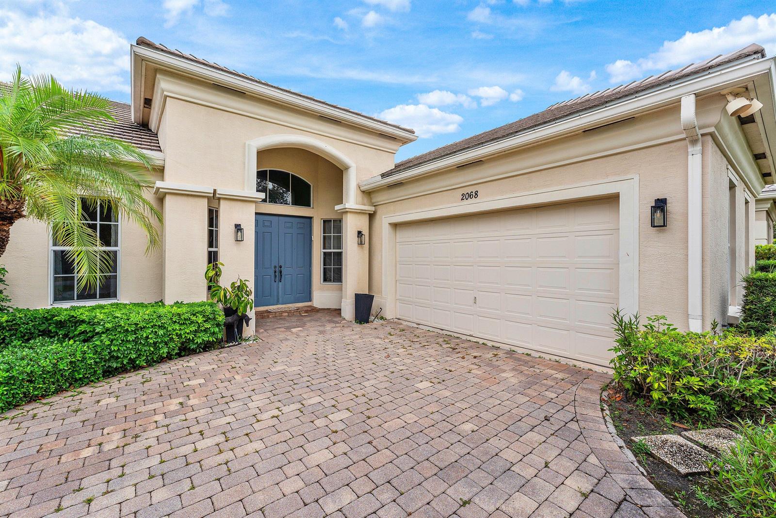 The exterior of a beige house features a blue double door and a paved driveway — 2068 Wightman Drive, Wellington FL 33414, WELLINGTON, FL