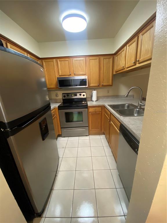 A galley kitchen features stainless steel appliances, wood cabinetry, and light-colored tile flooring — 5166 SUNRIDGE PALMS DRIVE, TAMPA, FL