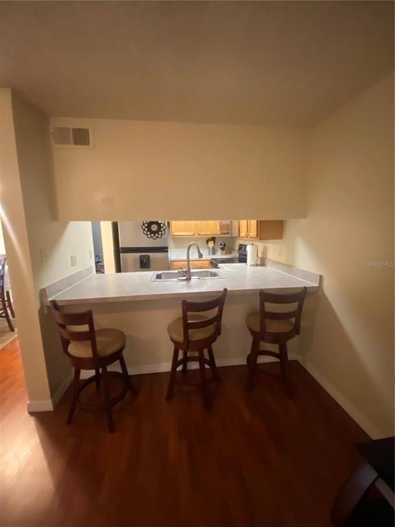 A kitchen pass-through window overlooks a breakfast bar with three wooden stools and wood flooring — 5166 SUNRIDGE PALMS DRIVE, TAMPA, FL