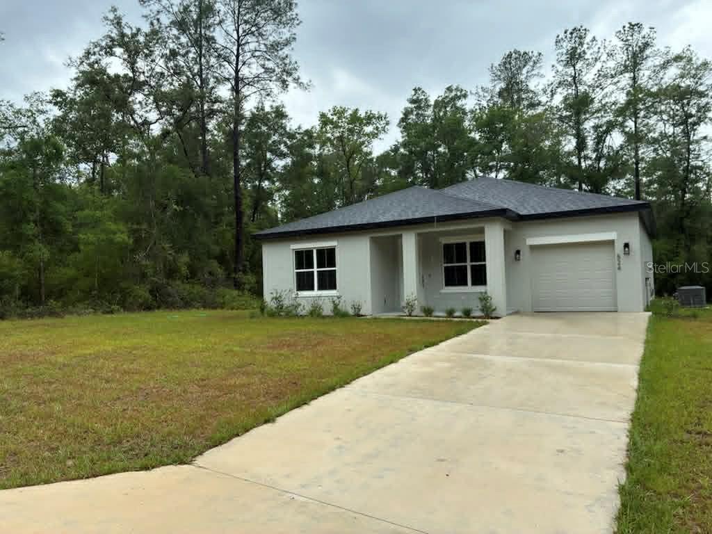 A single-story house with a concrete driveway, a one-car garage, and a wooded background — 524 E AVONDALE DRIVE, DUNNELLON, FL