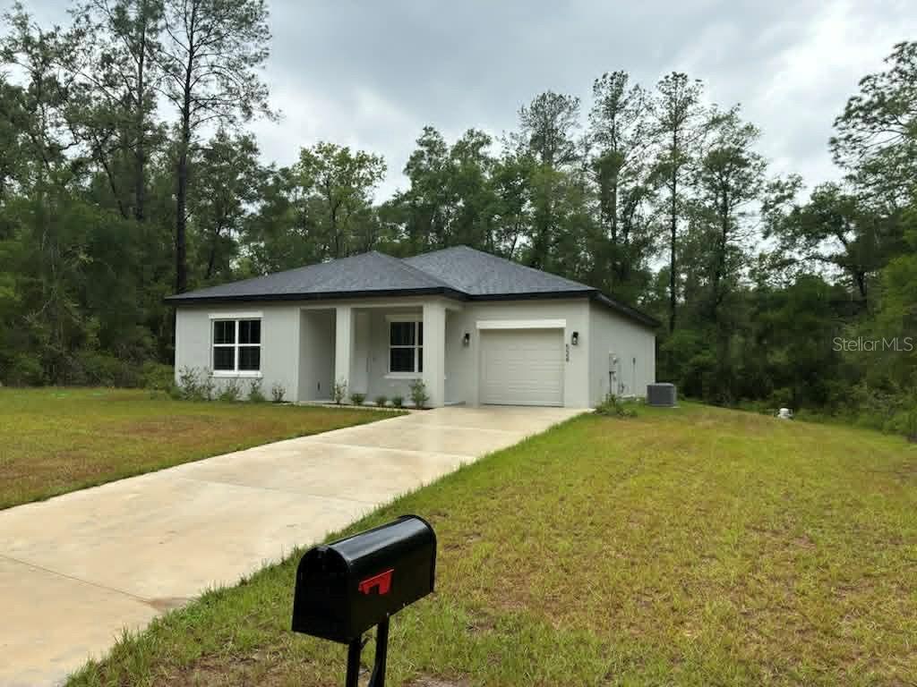 A single-story house with a gray roof, light-colored stucco exterior, and a concrete driveway — 524 E AVONDALE DRIVE, DUNNELLON, FL