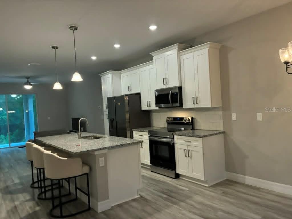 A modern kitchen features white cabinets, granite countertops, stainless steel appliances, and a center island — 524 E AVONDALE DRIVE, DUNNELLON, FL