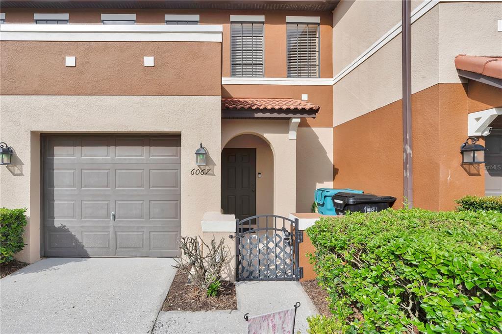 The exterior of a two-story townhouse features a garage, a gated entryway, and stucco siding — 6067 APOLLOS CORNER WAY, ORLANDO, FL