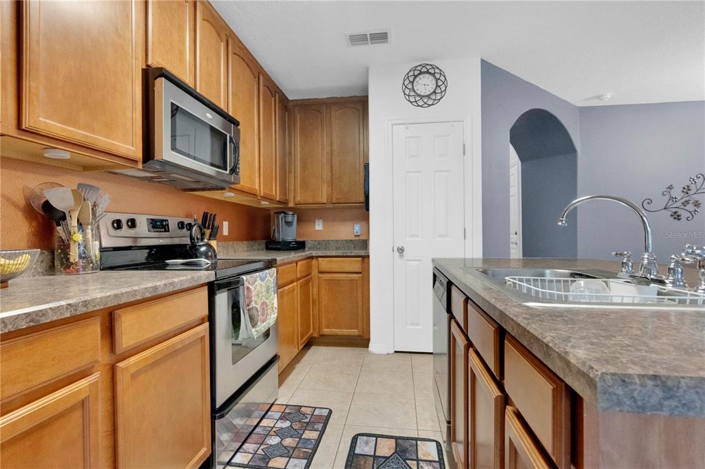 A kitchen features wood cabinets, stainless steel appliances, a center island, and tile flooring — 6067 APOLLOS CORNER WAY, ORLANDO, FL