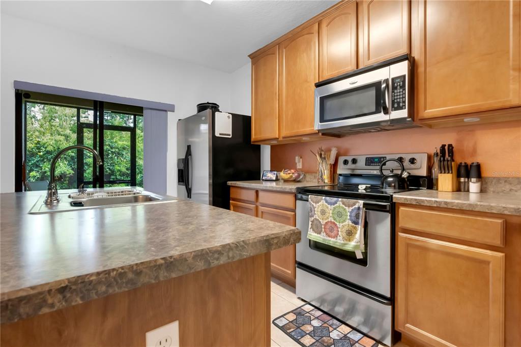 A kitchen features wood cabinets, stainless steel appliances, a laminate countertop, and a sliding glass door — 6067 APOLLOS CORNER WAY, ORLANDO, FL