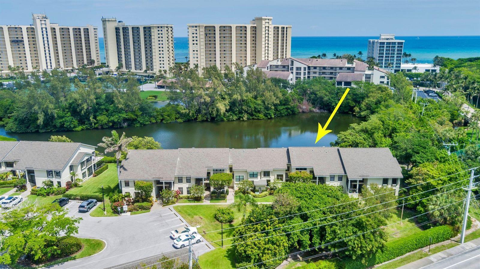 An aerial view shows a multi-unit residential building situated beside a lake and trees — 2306 FAIRWAY Drive S, Jupiter FL 33477, JUPITER, FL