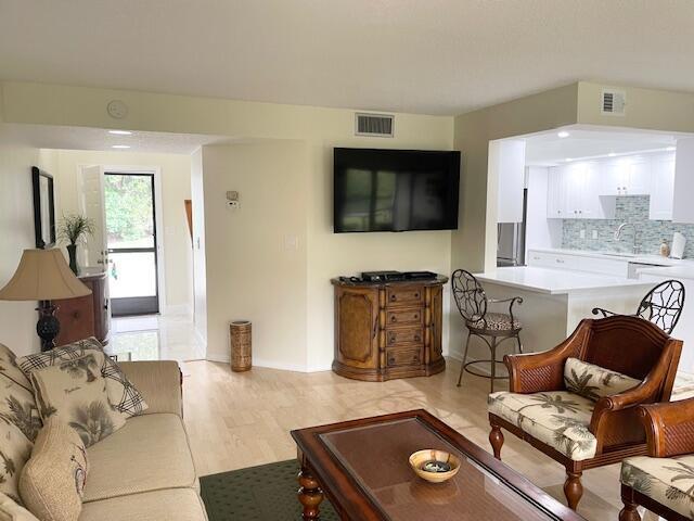 A living room with a television, wooden cabinet, and an open kitchen with white cabinets — 2306 FAIRWAY Drive S, Jupiter FL 33477, JUPITER, FL