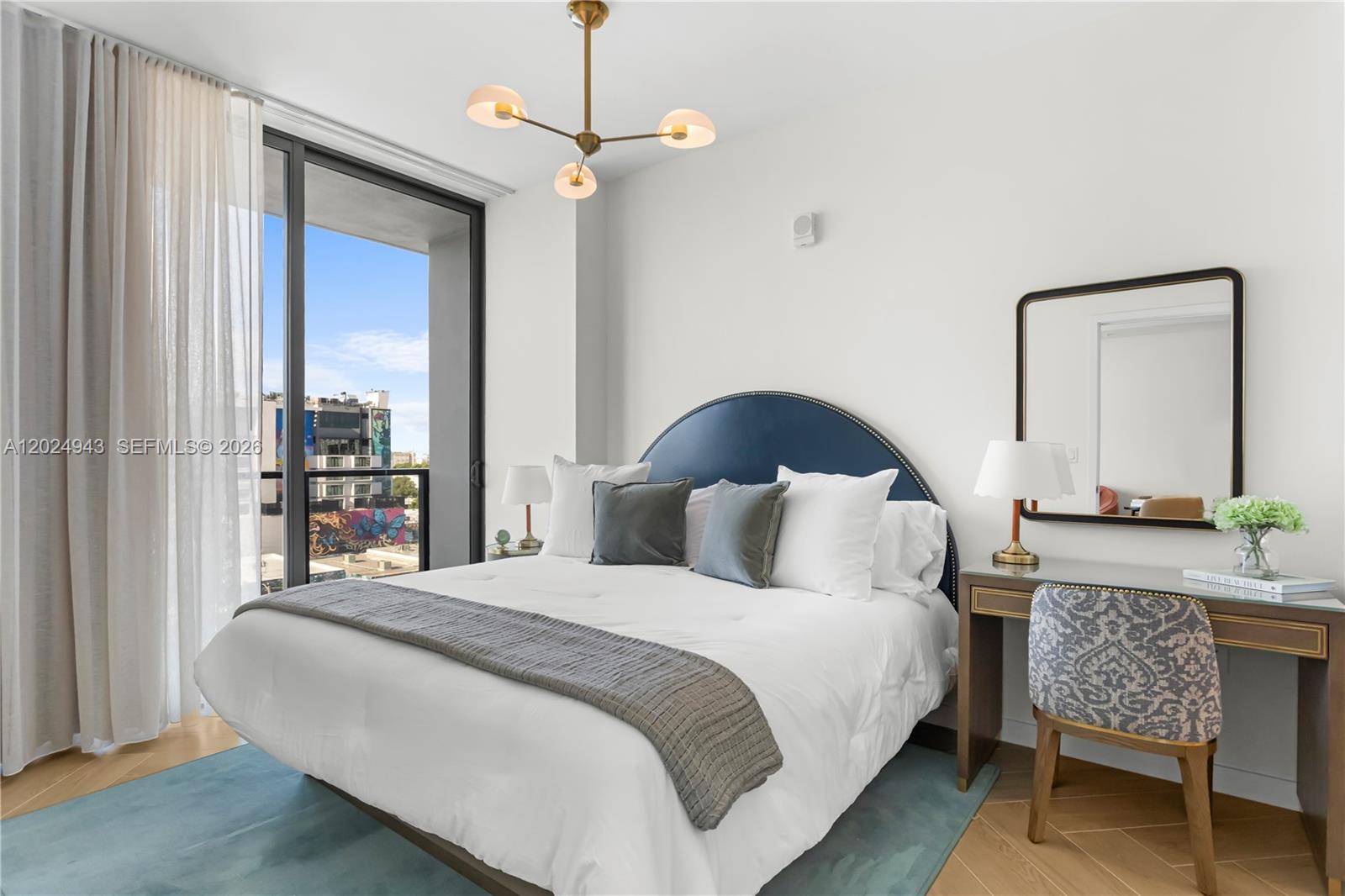 A bedroom features a blue headboard, a desk with a patterned chair, and a balcony view — 2700 NW 2nd Ave # 710, Miami FL 33127, MIAMI, FL