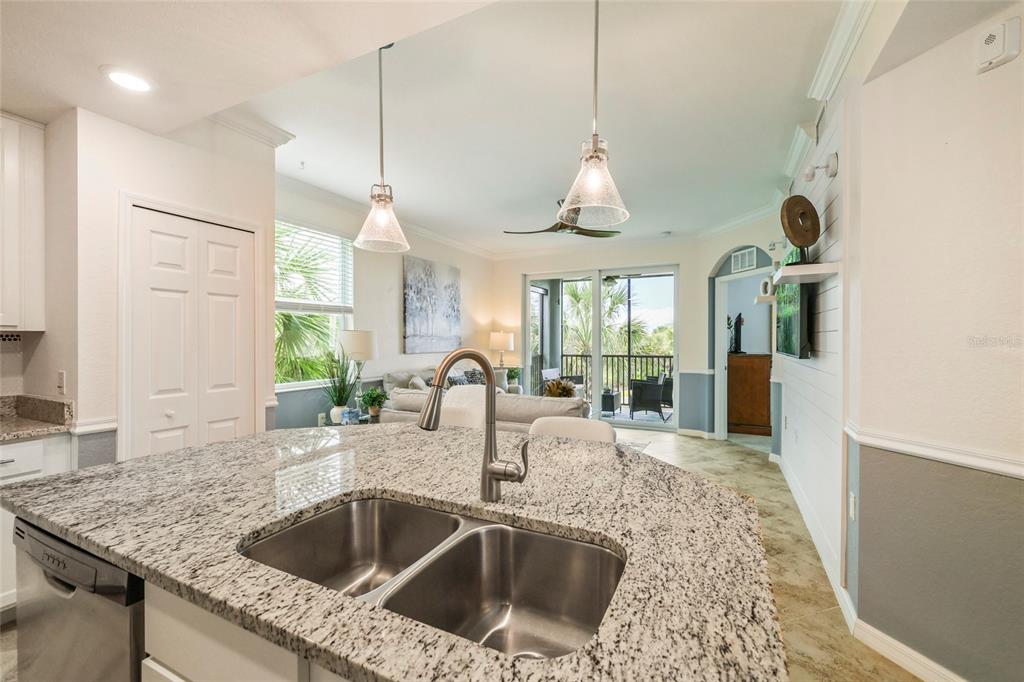 A kitchen island with a granite countertop and stainless steel sink overlooks a living area — 14091 HERITAGE LANDING BOULEVARD UNIT 121, PUNTA GORDA, FL