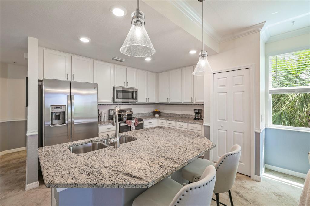 A kitchen with white cabinets, granite countertops, stainless steel appliances, and a central island — 14091 HERITAGE LANDING BOULEVARD UNIT 121, PUNTA GORDA, FL