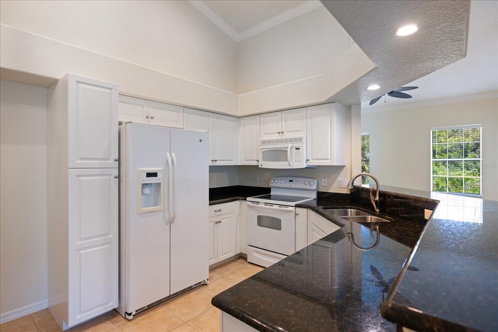 A kitchen features white cabinets, dark granite countertops, a white refrigerator, and a white stove — 300 GARDENS EDGE DRIVE UNIT 324, VENICE, FL