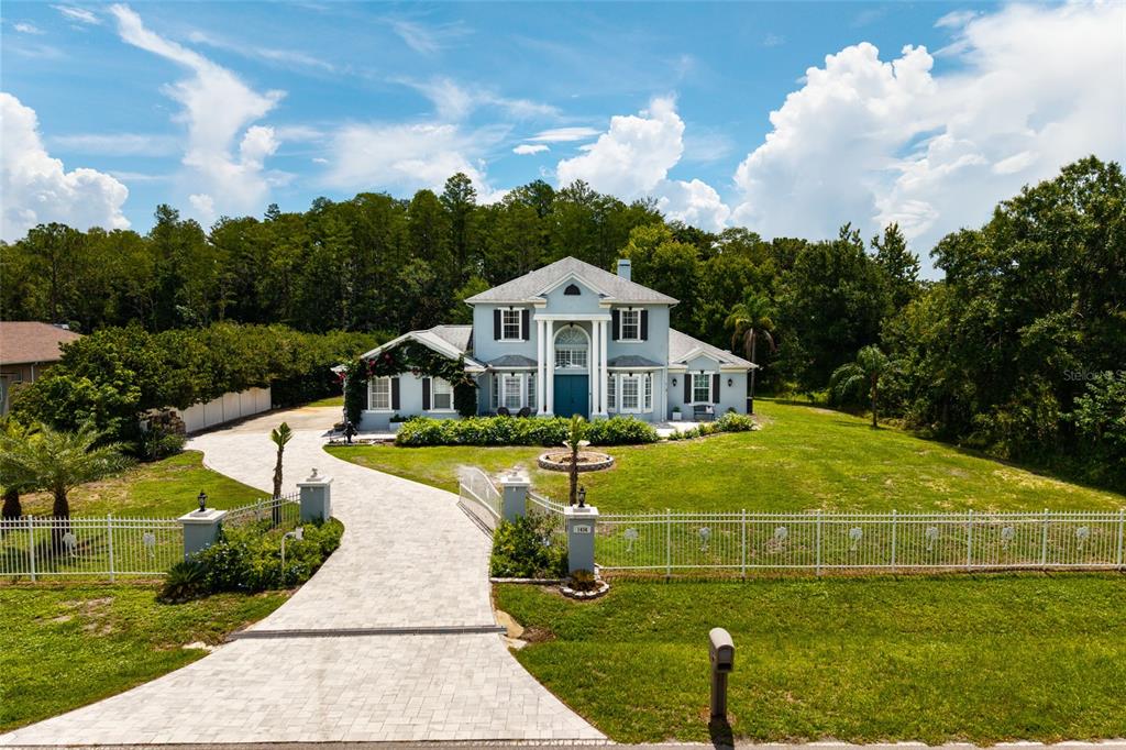 A two-story house with a paved driveway and gated entrance sits under a blue sky — 1436 ALTAMONT LANE, ODESSA, FL