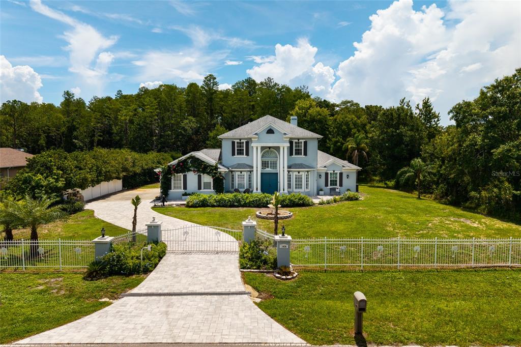 A two-story blue house with white columns sits behind a gated driveway and white fence — 1436 ALTAMONT LANE, ODESSA, FL