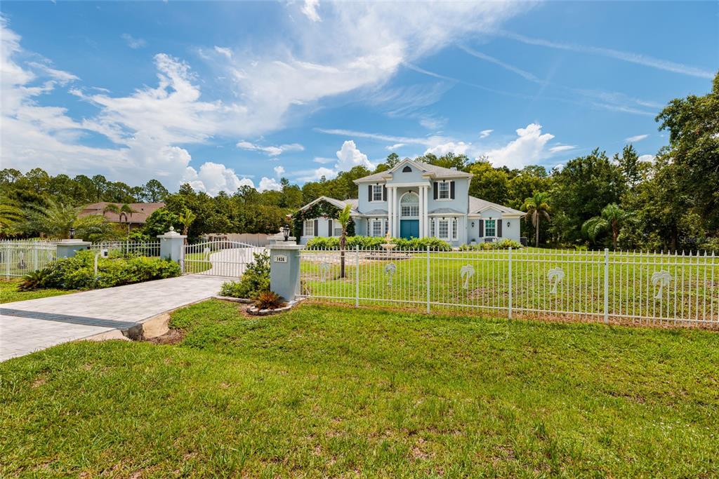 A two-story house with a white fence and a paved driveway sits on a lawn — 1436 ALTAMONT LANE, ODESSA, FL