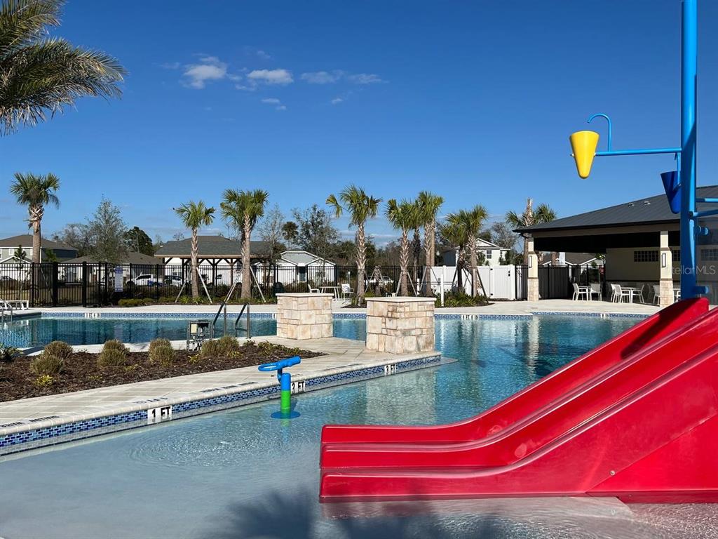 A swimming pool with a red slide and a covered patio area under a blue sky — 1248 WISPY CYPRESS DRIVE, KISSIMMEE, FL