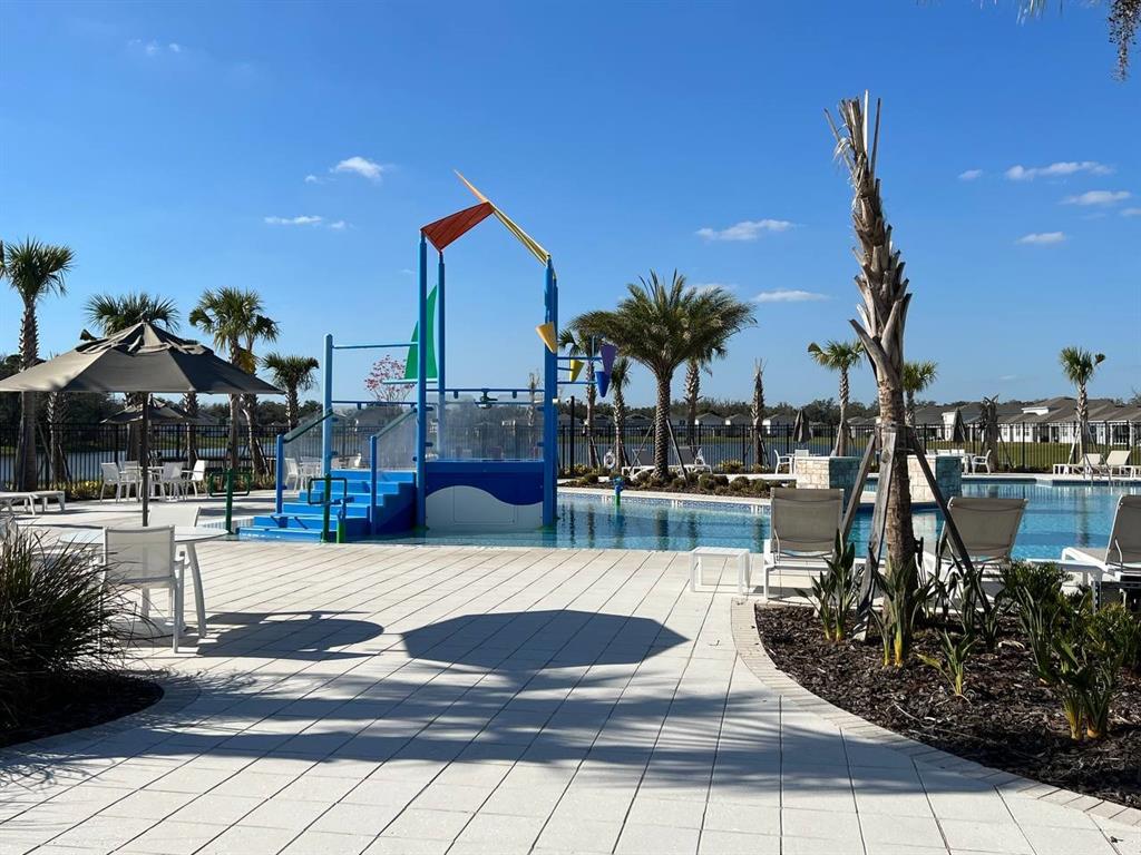 A swimming pool area features a colorful water play structure, lounge chairs, and palm trees — 1248 WISPY CYPRESS DRIVE, KISSIMMEE, FL